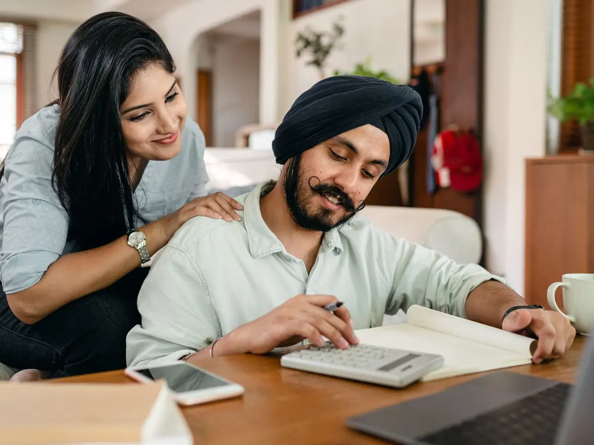 A couple at home working through their finances with a calculator, notebook and laptop