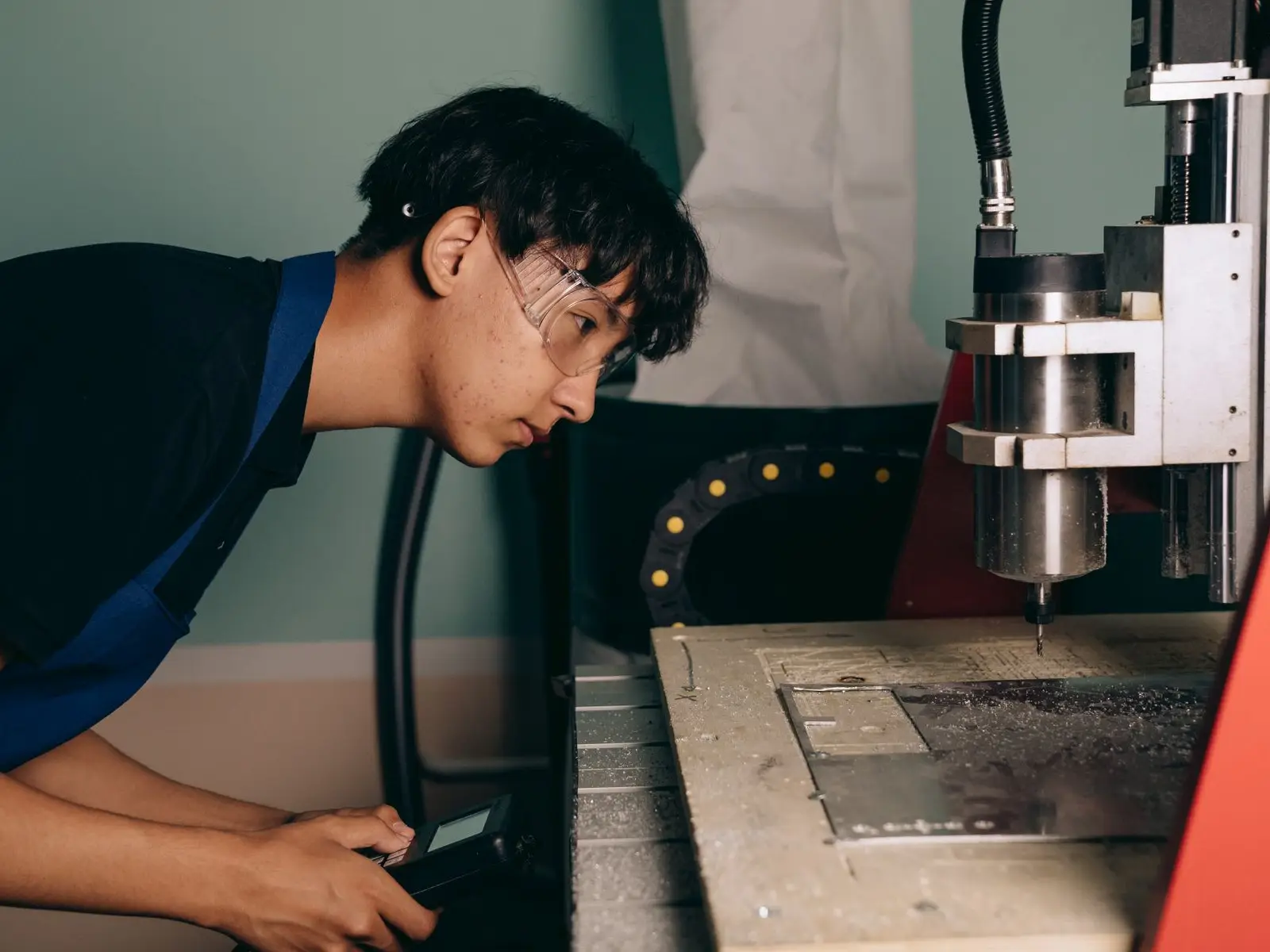 An engineering student in safety glasses operating a CNC machine in a workshop
