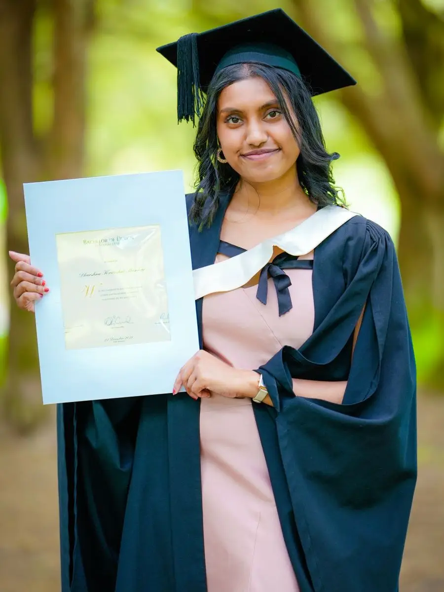 Prakriti in a graduation cap and gown, holding her degree certificate