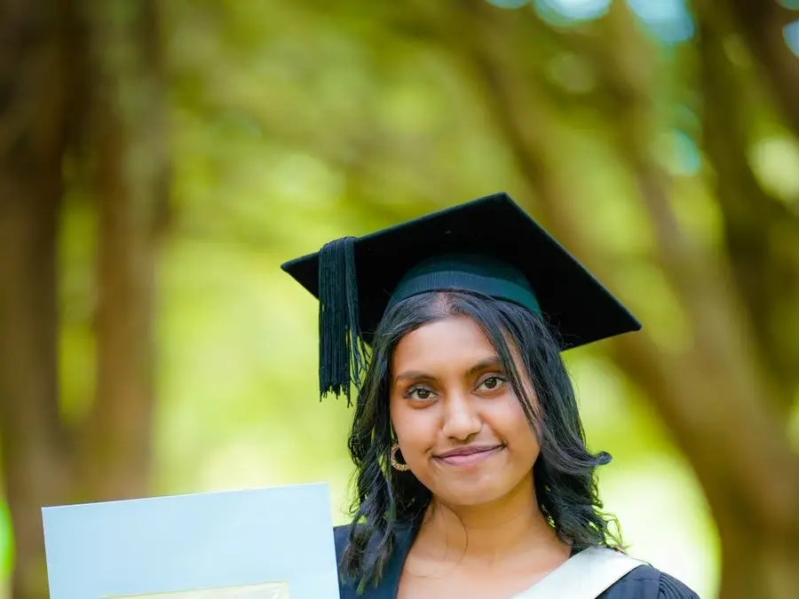 A Nepali nursing graduate in cap and gown holding a degree certificate