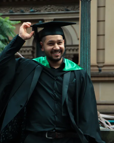 A graduate in cap and gown celebrating outside a university building in Sydney