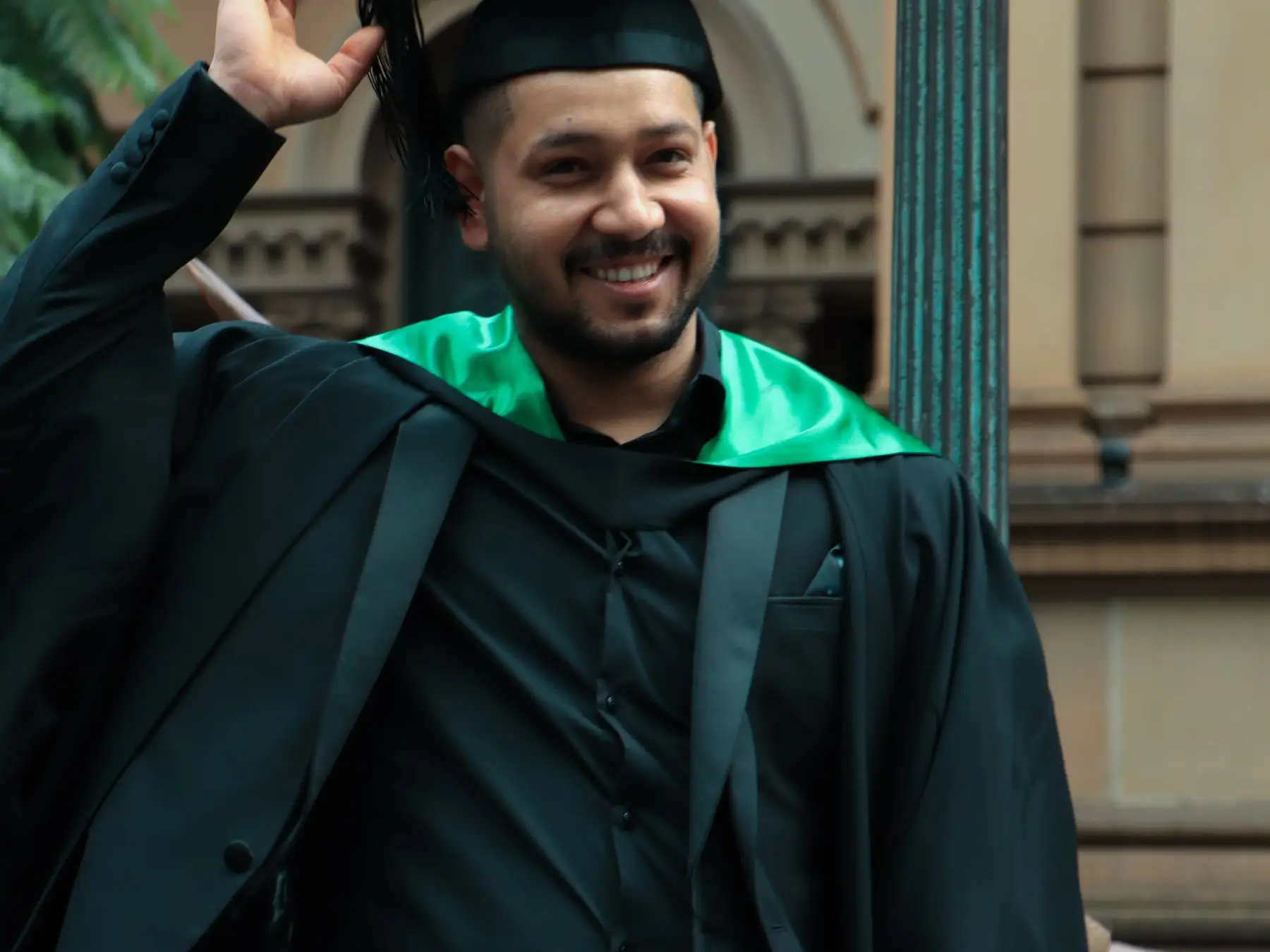A graduate in cap and gown celebrating outside a university building in Sydney
