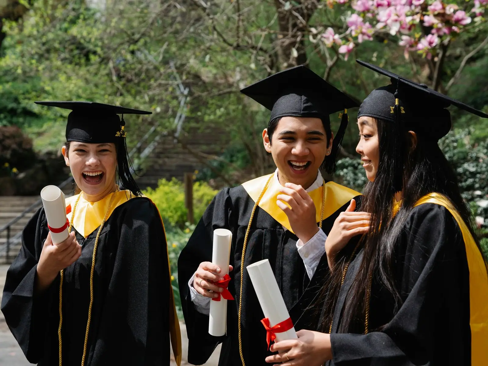 Three smiling graduates in caps and gowns holding their degree scrolls