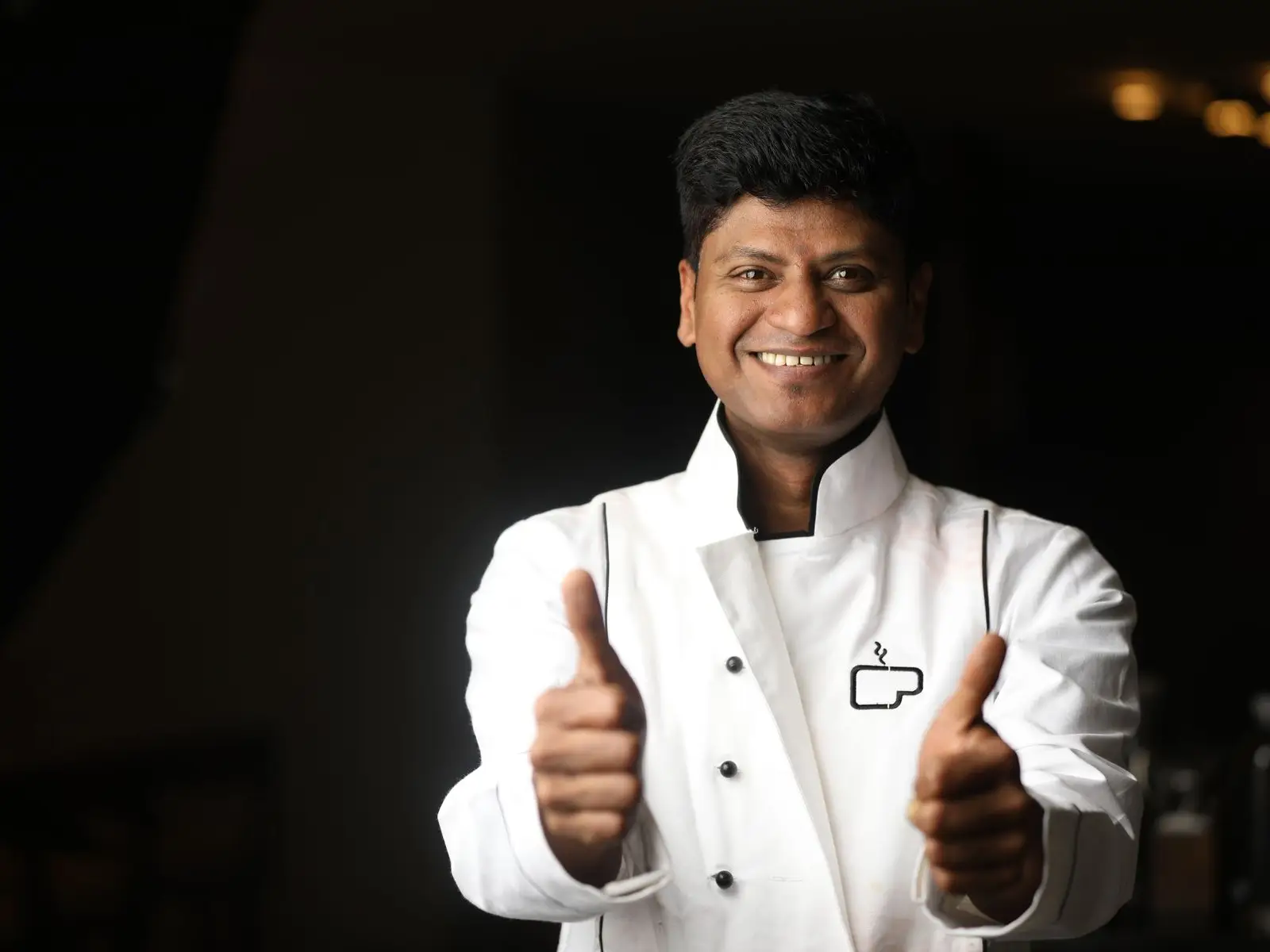 A smiling chef in whites giving two thumbs up