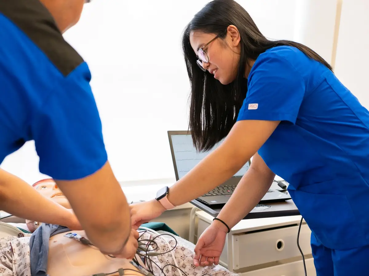 Two nursing students in blue scrubs practising on a mannequin in a simulation lab