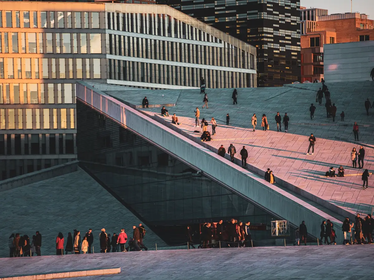 People walking on the sloping roof of the Oslo Opera House at sunset