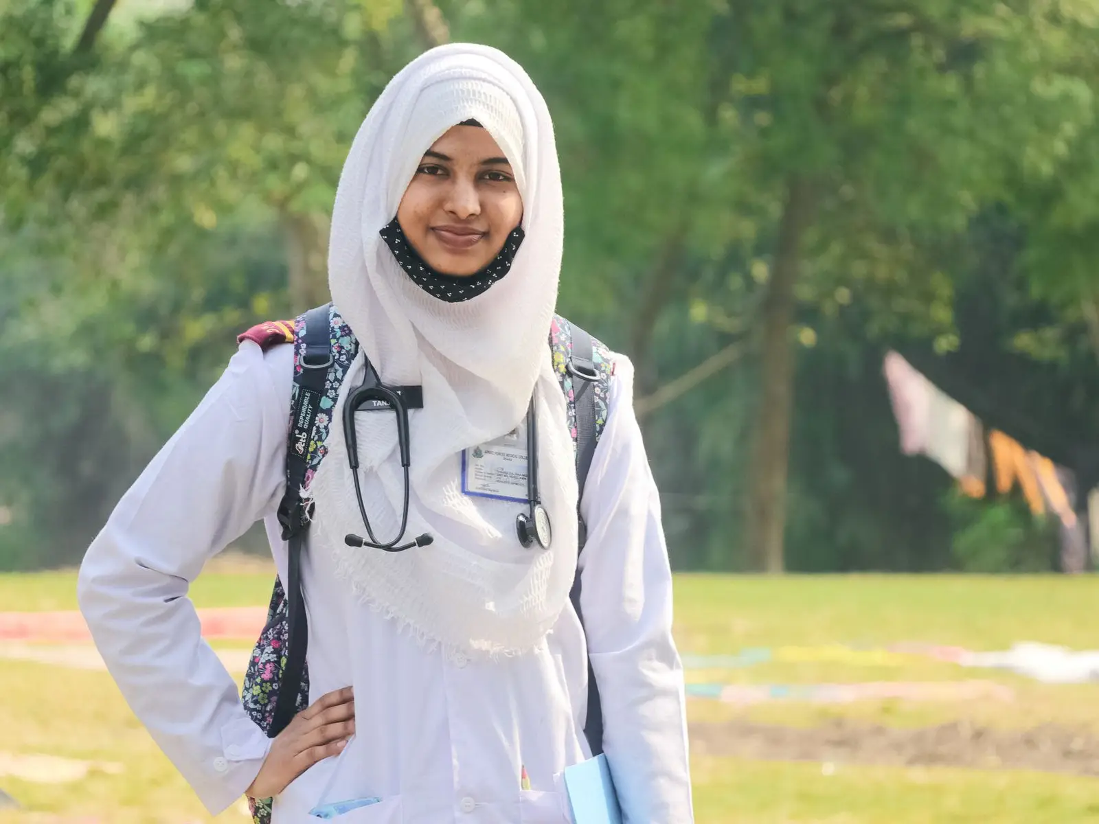 A smiling young doctor with a stethoscope and backpack, standing outdoors