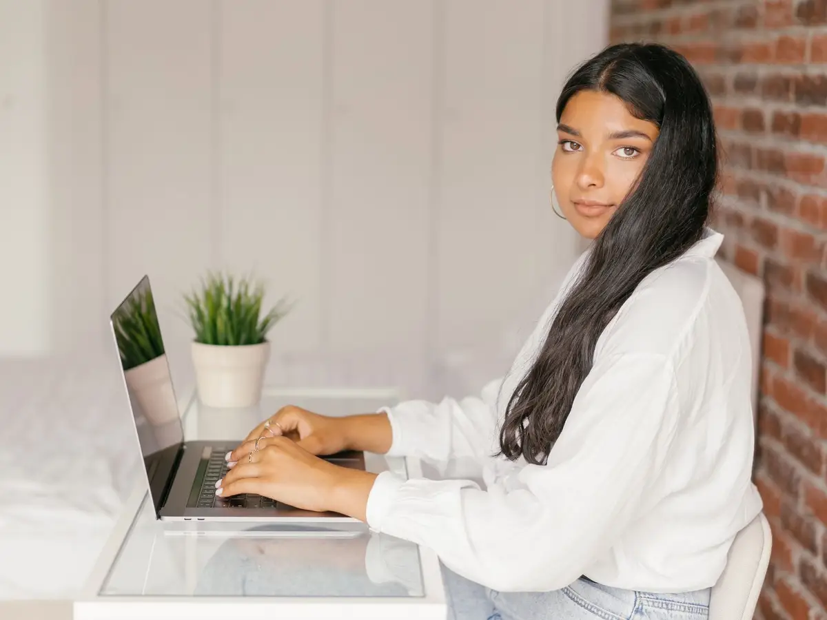 A young woman at a desk at home, typing on a laptop