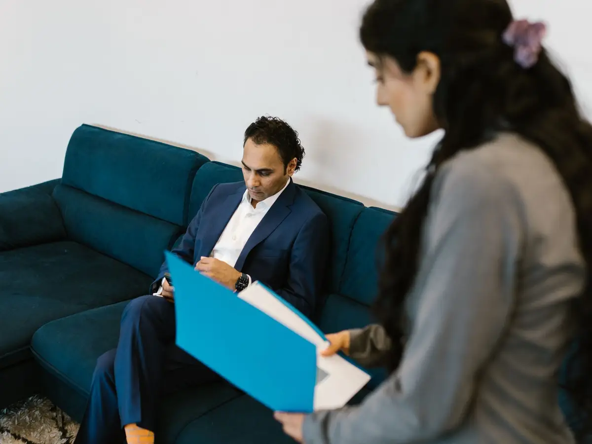 A student going through a blue folder of papers with a counsellor on an office sofa