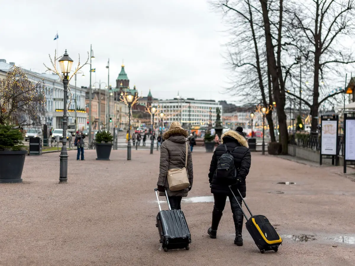 Two people wheeling suitcases along a street in Helsinki on a grey winter day