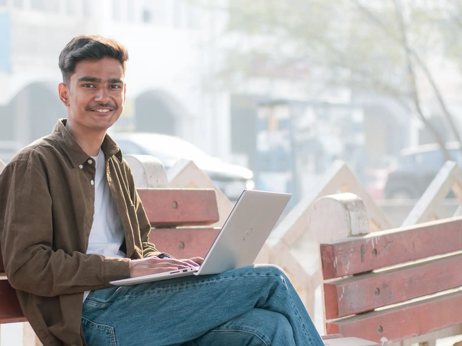 A student smiling on a park bench, practising on a laptop